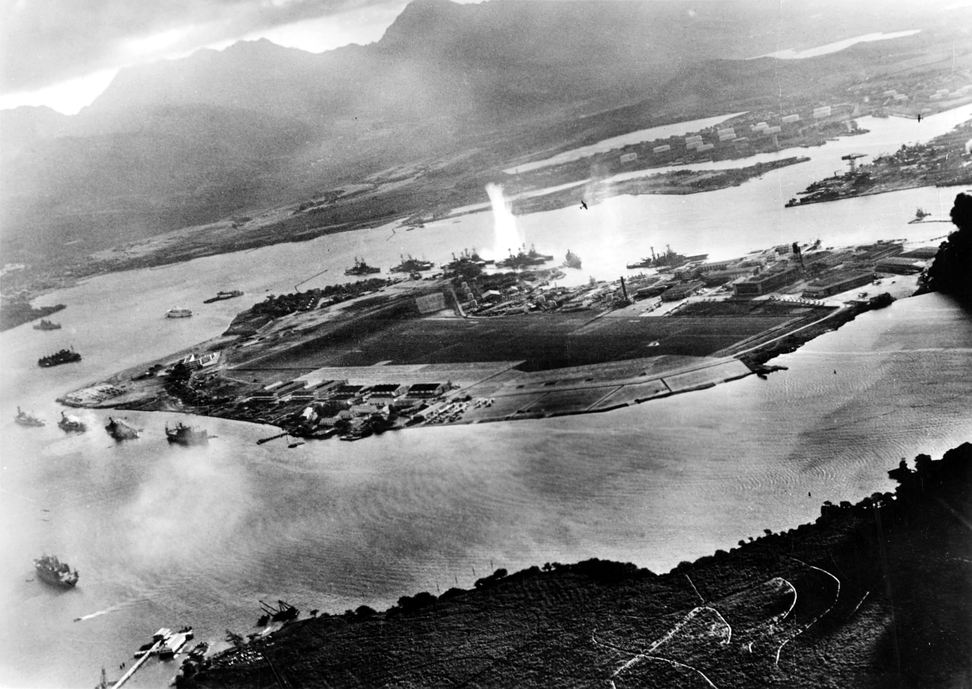 Photograph taken from a Japanese plane during the torpedo attack on ships moored on both sides of Ford Island shortly after the beginning of the Pearl Harbor attack. View looks about east, with the supply depot, submarine base and fuel tank farm in the right center distance.
A torpedo has just hit USS West Virginia on the far side of Ford Island (center). Other battleships moored nearby are (from left): Nevada, Arizona, Tennessee (inboard of West Virginia), Oklahoma (torpedoed and listing) alongside Maryland, and California.
On the near side of Ford Island, to the left, are light cruisers Detroit and Raleigh, target and training ship Utah and seaplane tender Tangier. Raleigh and Utah have been torpedoed, and Utah is listing sharply to port.
Japanese planes are visible in the right center (over Ford Island) and over the Navy Yard at right. U.S. Navy planes on the seaplane ramp are on fire.

Japanese writing in the lower right states that the photograph was reproduced by authorization of the Navy Ministry.