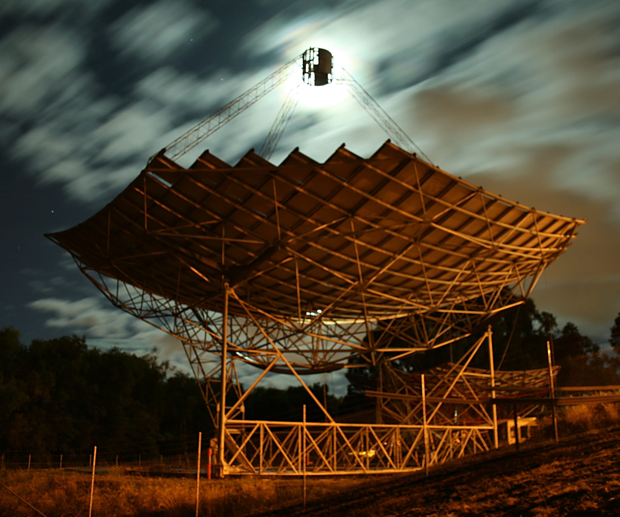 Night exposure of a paraboloidal solar concentrator located at the Australian National University.  The moon is behind the focus and is illuminating fast moving clouds.