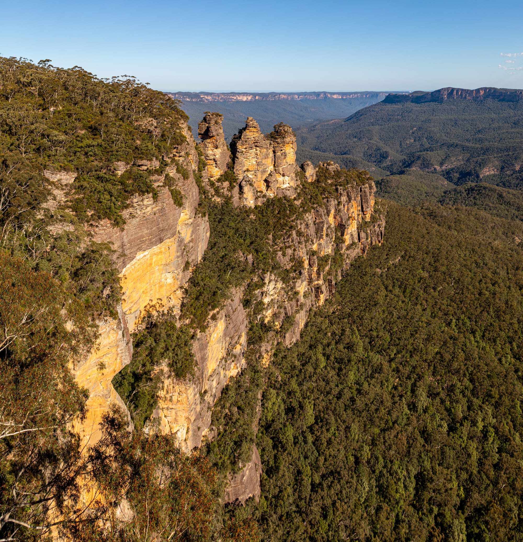 Three Sisters, Blue Mountains National Park, New South Wales, AustraliaThe Blue Mountains National Park is located west of Sydney and is one of Australia’s most famous natural areas. Its history is closely linked to Aboriginal culture, particularly that of the Gundungurra and Darug peoples, who have inhabited the area for tens of thousands of years and have a spiritual connection to the landscape.For European settlers, the rugged sandstone plateaus were long considered an insurmountable obstacle. It was not until 1813 that Gregory Blaxland, William Lawson, and William Charles Wentworth succeeded in crossing the mountains, opening the way for the development of the Australian hinterland.In the 19th century, parts of the region were used for logging and mining, while at the same time its scenic appeal was discovered. In 1959, the Blue Mountains National Park was officially established to protect the unique eucalyptus vegetation, deep gorges, and waterfalls.In 2000, UNESCO declared the area part of the Greater Blue Mountains Area a World Heritage Site. Today, the park stands for nature conservation, tourism, and recognition of Australia’s indigenous cultural history.