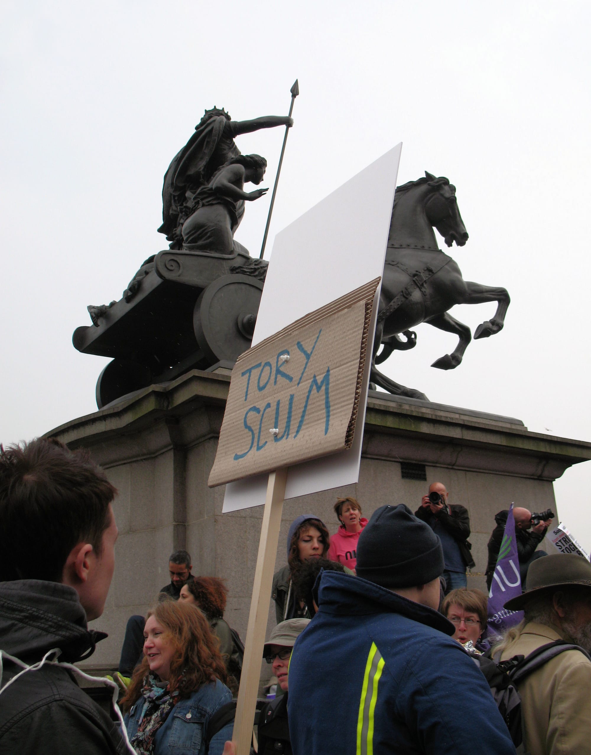 Protesters, one with a placard with the words "Tory scum" written on it. In the background is the statue of Boadicea and Her Daughters, which is in Westminster, London. The protesters were part of the TUC's anti-austerity March for the Alternative on 26 March 2011.
