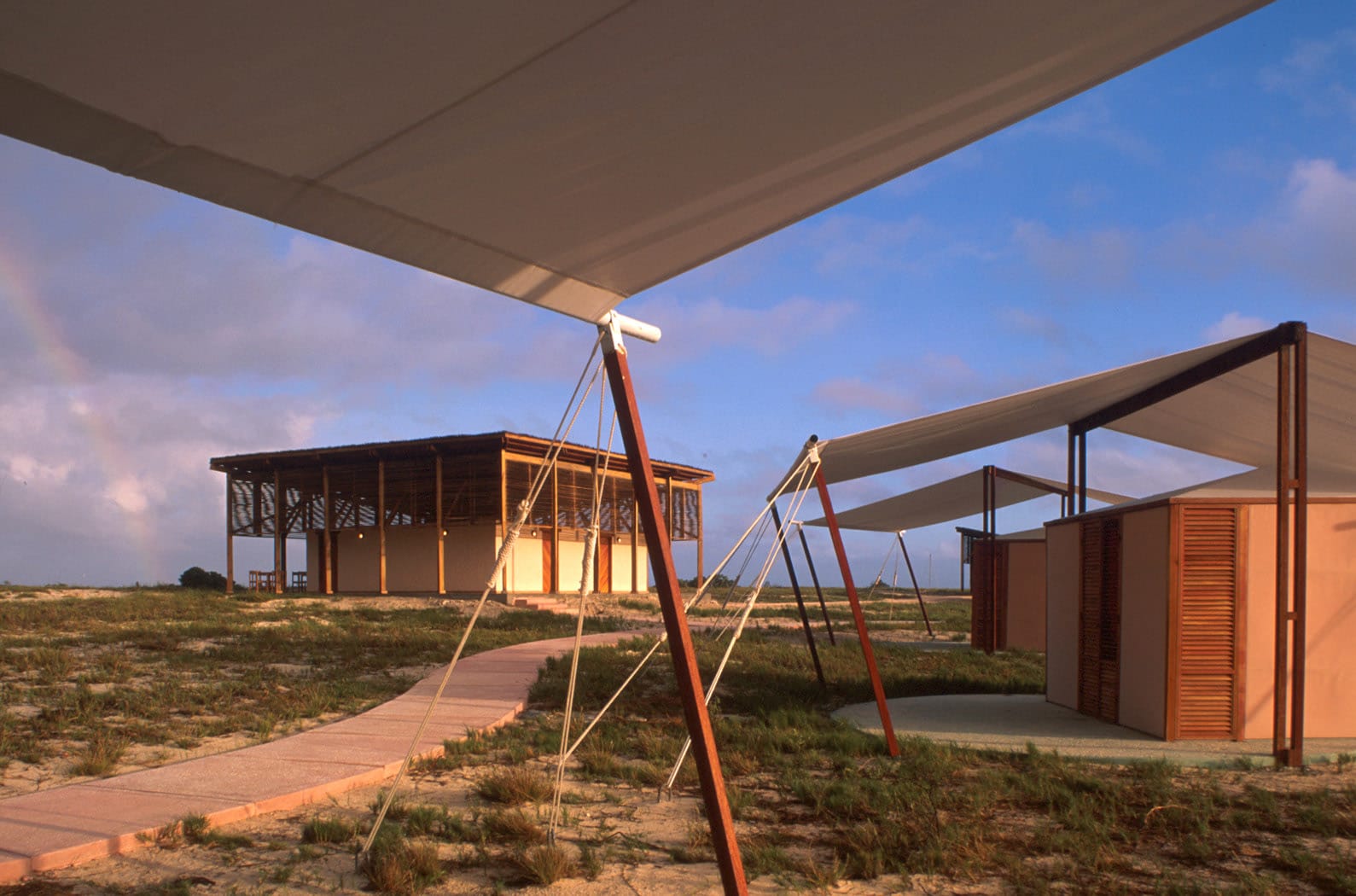 Cayo Crasqui Ecological Tourism Camp from Venezuelan architect Jorge Rigamonti. The photo shows the tents composed of double tops, double canvas walls, and wooden venetian blind doors and windows, which provide cover from the intense sun and ventilation for natural climatic comfort. The tents and the services building in the distance are built from biodegradable materials (wood and canvases) for low environmental impact.
