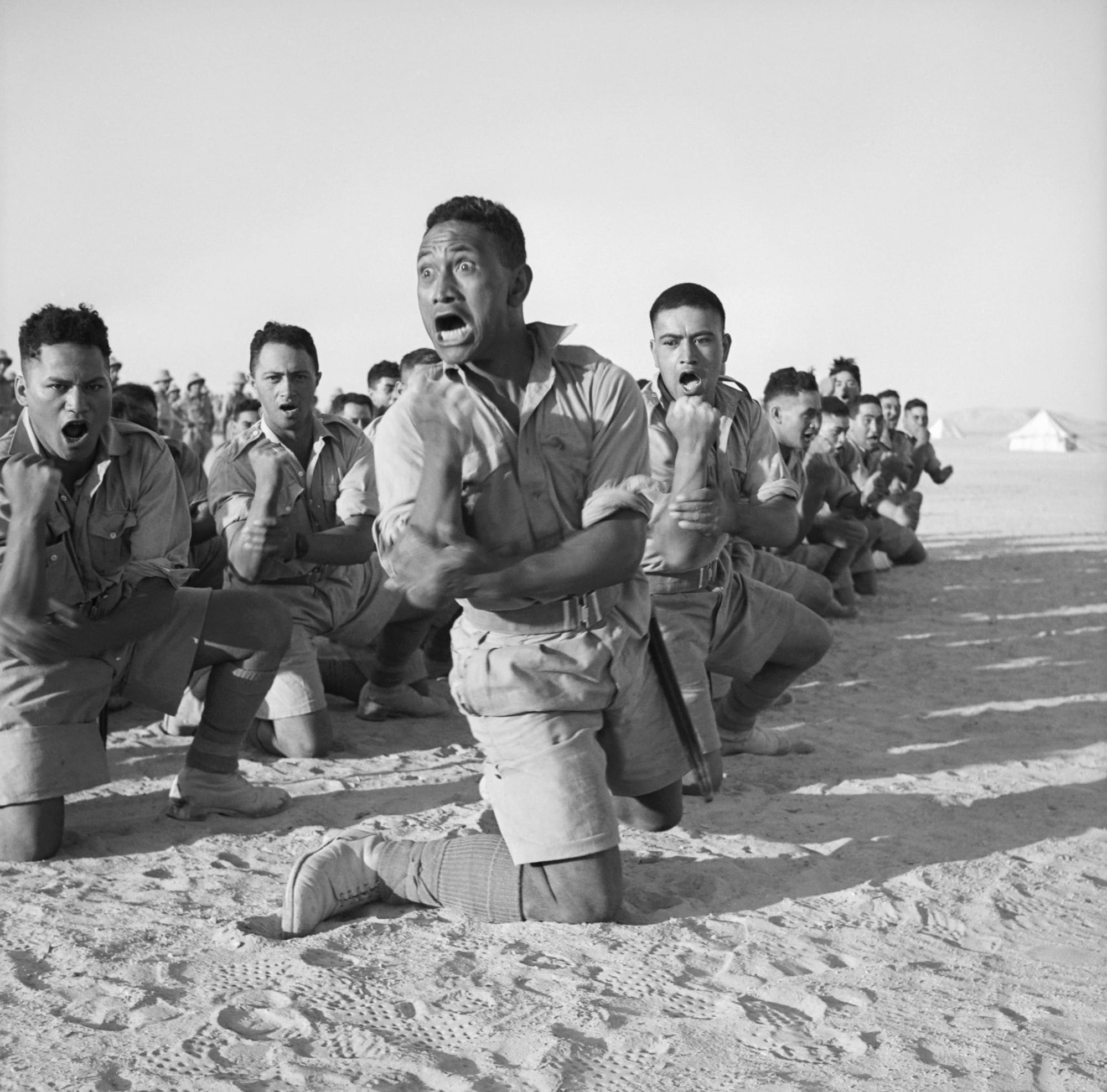 Māori Battalion survivors of action in Greece, performing a haka in Helwan, Egypt for the King of Greece. From left to right, the four men in the foreground are John Manuel, Maaka White, Te Kooti Reihana, and Rangi Henderson.A cropped version of this photo featured on an ANZAC commemorative stamp issued in 2008.[2]