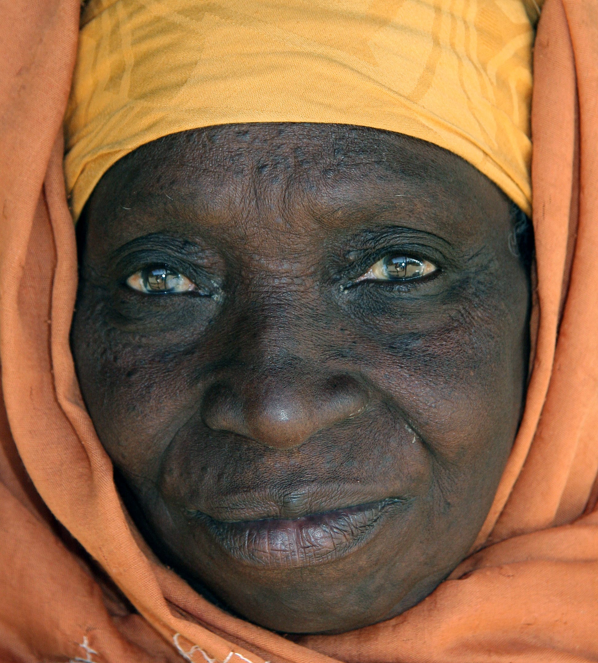 Elderly Gambian woman's face surrounded by yellow and orange hijab. January 2008, The Gambia.
