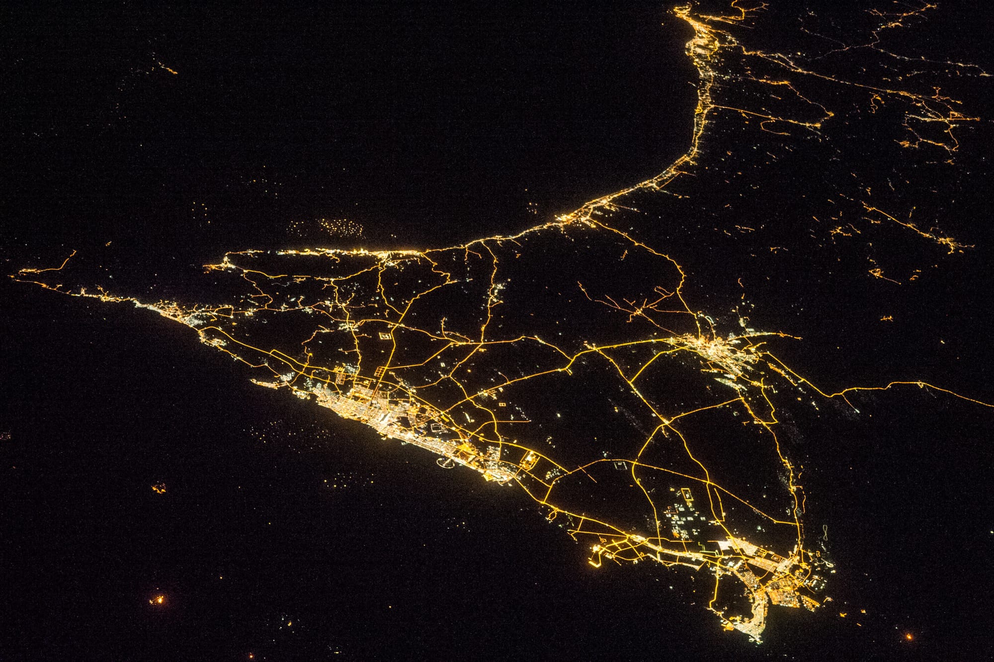 A nighttime view of the United Arab Emirates is featured in this image photographed by an Expedition 38 crew member on the International Space Station.
Geographers like night images of cities because you see immediately so much about the human landscape–things that are difficult or impossible to see in day images. You see where the cities are located and their shape; the brightest light clusters frequently indicate the city centers.
In large field of view images, such as this photograph of the United Arab Emirates (UAE), you can also see cities' position relative to one another and their relative size. Here the largest cluster of lights is the conurbation ("joined cities") of Dubai-Sharjah-Ajman (population 3.25 million), with its smaller neighbor Dubai (population 2.1 million). These cities front onto the Persian Gulf (also known as the Arabian Gulf) where the city lights are cut off abruptly at the coastline. The bright city centers are located at the coast showing that sea trade is important (and has been important) in the growth of these cities.
Smaller cities are Al Ain (population 518,000), the fourth largest city in the UAE, and Fujairah (population 152,000). Major highways join the cities in a brightly lit network, and a faint peppering of lights offshore shows the relatively young oil and gas platforms on either side of the Musandam Peninsula (left). Despite being taken at night, the spike of the Musandam Peninsula is easy to imagine at the south end of the Persian Gulf. The biggest cities in the UAE are Abu Dhabi and Dubai.
Muscat, the capital city of the neighboring country of Oman, appears top center. By contrast, the almost unpopulated Musandam Peninsula shows very few lights.