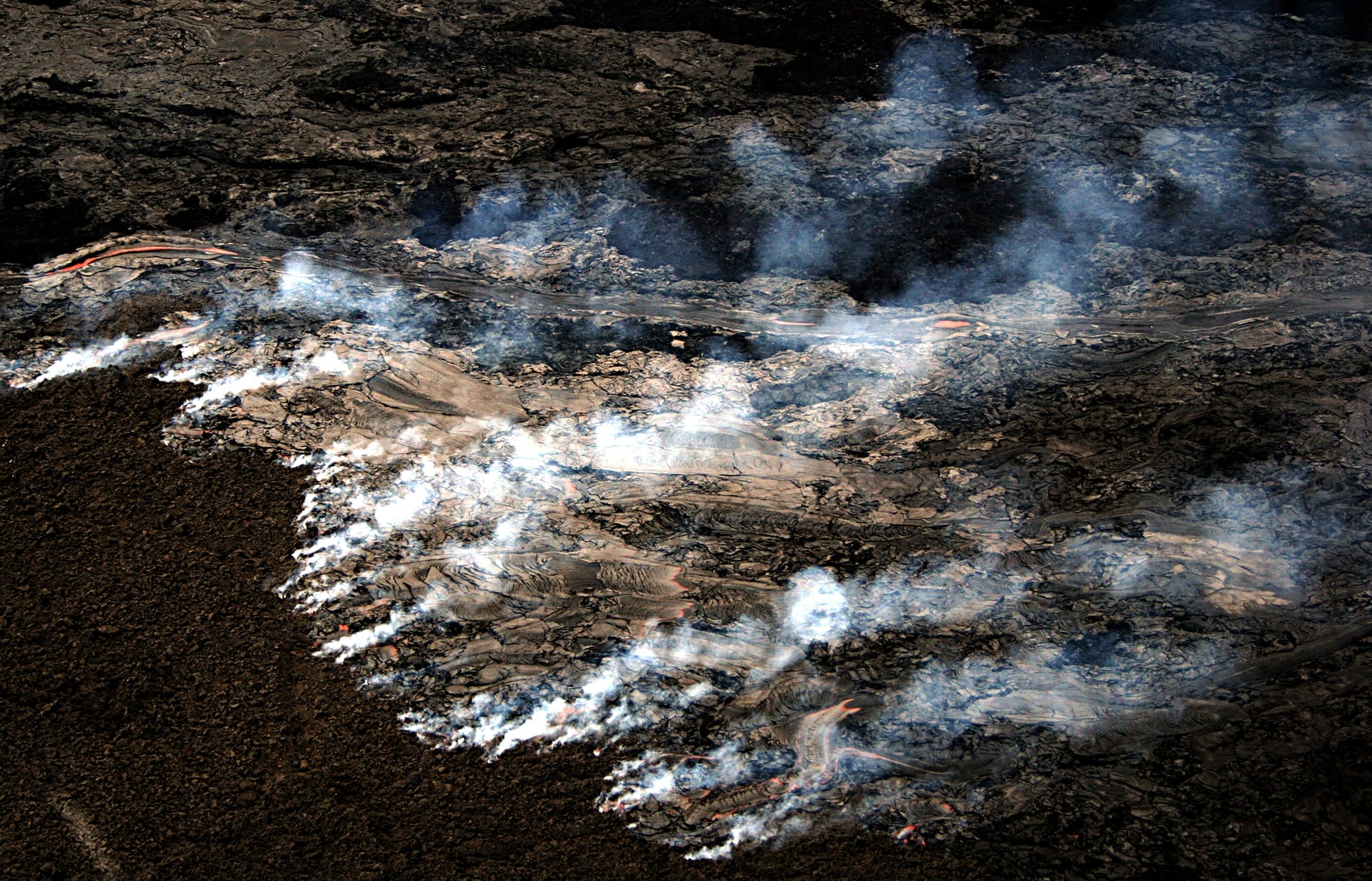 Pāhoehoe Lava flow on the coastal plain of Kīlauea, The Big Island of Hawai generated wildfire. The new lava is moving across the old surface, which is covered with a layer of moss about an inch thick. This moss is burning generating the smoke visible in the image. This kind of fire cannot be easily prevented or suppressed. The update that was written by USGS for the same day the image was taken - 09/04/07 says :"Lava flows advancing through vegetation are hazardous and can produce fire and methane explosions that propel chunks of lava and rock several feet into the air." The picture was taken from a helicopter.