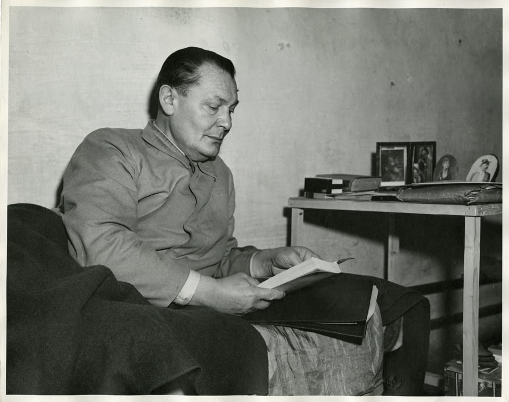 Commander of the Luftwaffe Hermann Göring, photographed in his jail cell at Nuremberg, Germany, during the Nuremberg Trials. Göring is seen reading a book while lying on his bed in his cell next to a table with photos of his daughter Edda Göring, his wife Emmy Göring, and his parents Franziska and Heinrich Ernst Göring. Gelatin silver process on paper. 28 x 35.3 cm. Image courtesy of the Harvard Law School Library, Harvard University, Cambridge, Mass.