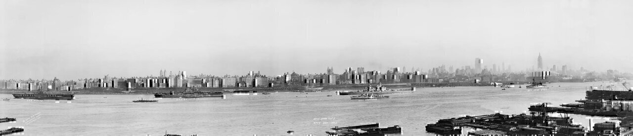Panorama of Manhattan's West Side from Across the Hudson, celebrating Navy Day and the end of the Second World War, showing ships at harbor including the U.S.S. Midway, the largest ship in the world at the time. Vintage silver gelatin photograph.
Sweeping from left to right, the ships shown include the U.S.S. Midway, the U.S.S. Enterprise, the U.S.S. Isherwood, the Flagship Missouri, the U.S.S. New York, and the U.S.S. Helena.
In the background, the western side of Manhattan is seen to extend just north of the Grant Memorial Soldiers' and Sailors' Monument and as far south as the Empire State Building. The view of the skyline is crisp, with all individual buildings recognizable.
In the foreground, New Jersey's docks, including those of the United Africa Company, can be seen.
Navy Day, a holiday to celebrate the US's naval armed forces, was established in October 1922. The 1945 Navy Day was the first post-war Navy Day, and ships at fifty-six different berths celebrated the event.

This image was taken by Tom Blackmore of Larchmont, New York.