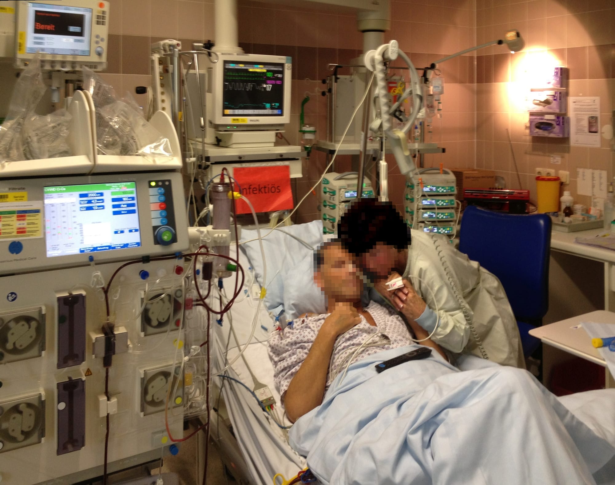 A patient is lying in a hospital bed in an intensive care unit of a hospital in Germany 2015. To the left is a hemodialysis machine, above the man is a monitor for heart rate and other parameters, to the right are apparatuses (infusion pumps) for administering medicine into the bloodstream. The standing person is a visitor. The orange sign says "Infektiös", which is German for "contagious". The persons on the picture were made unidentifiable by pixelization of the faces.The patient suffered from a very severe sepsis due to a prior surgery of the intestinal region for curing a less grave form of bowel cancer, from which he returned to his home too early, and after which grave spasms due to a food intolerance had led to a rupture in the region which had been treated during the surgery. This had induced multi-organ failure caused by a severe bacterial infection of the body between the hip region and the lungs, as the patient had returned to hospital only after two days during which he suffered from various symptoms. He had to have an emergency surgery. After subsequently spending two months in the intensive care unit and one further month in a specialized hospital department for kidney treatment, the patient had lost weight from 75 kg to less than 50 kg. He then left, fully recovered within weeks and is since then entirely well until present (2023), without any remains of the events other than the 20 cm long vertical operation scar on the chest.