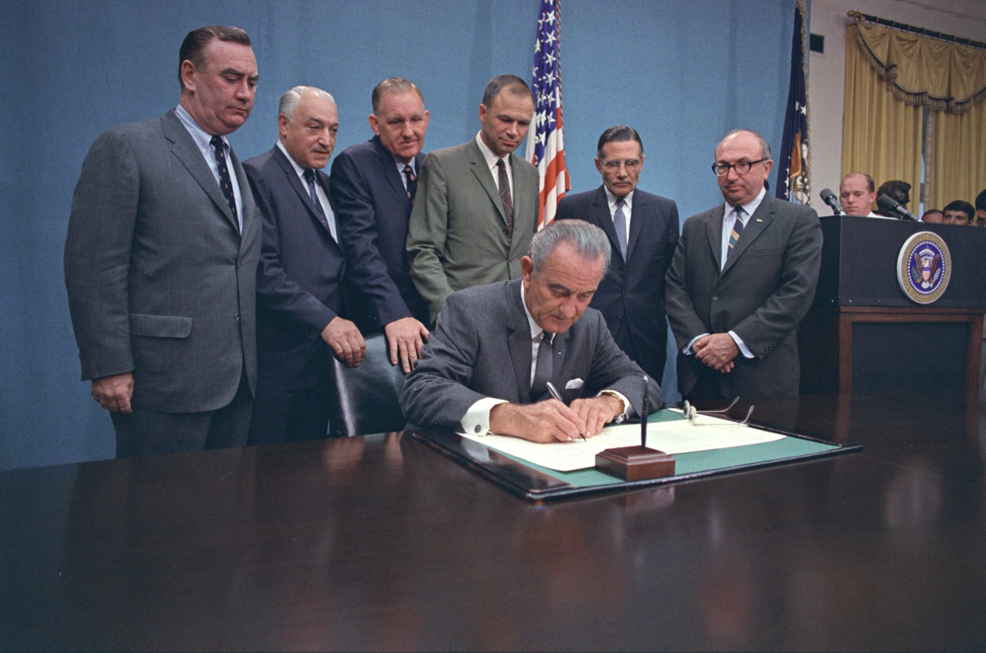 President Lyndon B. Johnson Signing H.R. 18763, the Bill to Authorize Pre-School and Early Education Programs for Handicapped Children. Original Caption: Standing (l-r): Cong. Hugh L. Carey, Cong. Dominick V. Daniels, Cong. Carl D. Perkins, Cong. Albert H. Quie, Sen. Winston L. Prouty, and Sec. Wilbur Cohen. 9/30/1968. Location: Cabinet Room, White House, Washington, DC.