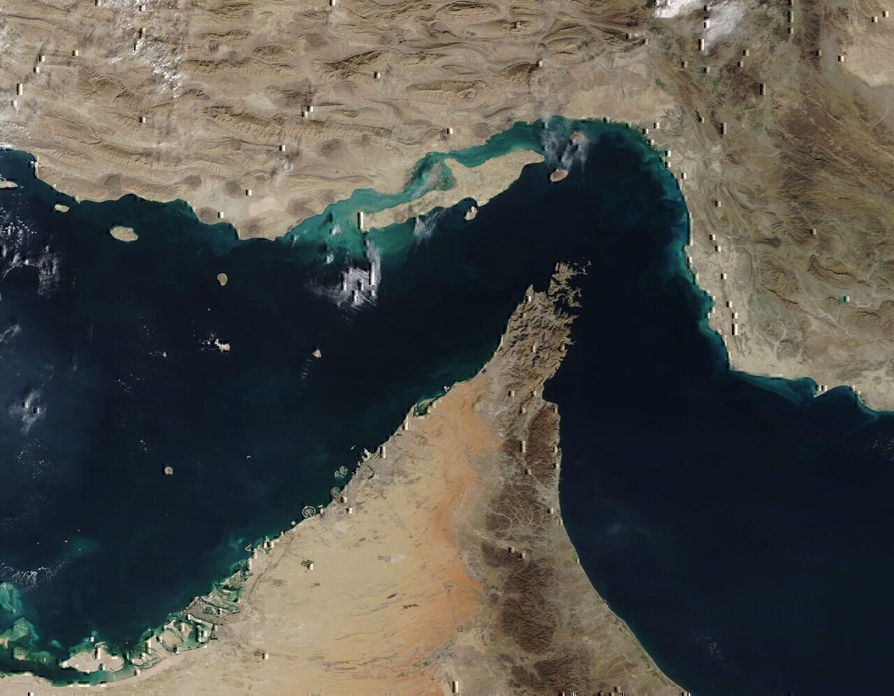 The narrow Strait of Hormuz lies between the Persian Gulf and the Gulf of Oman, separating Iran (north) from the Arabian Peninsula (south). Only about 21 miles (34 km) wide at the narrowest point and roughly 96 miles (155 km) long, about thirty percent of the world’s seaborne oil and nearly one-quarter of the liquified natural gas (LNG) supply passes through this strait — all on shipping lanes that measure only two-mile wide. It has been estimated that 21 million barrels of oil, with a value of 1.2 billion US dollars (USD), pass through the strait every day.
On December 2, 2020, the Moderate Resolution Imaging Spectroradiometer (MODIS) on board NASA’s Terra satellite acquired a true-color image of the Strait of Hormuz.

The arid landscape of Iran sits in the north, with Qeshm Island, the largest in the Persian Gulf, just off the Iranian coast. The tiny Strait of Khuran separates the island and the mainland and bounds a wetland of international importance, recognized by Ramsar. These wetlands provide critical habitat to two globally threatened species: the Dalmatian Pelican and the Green sea turtle. In the south, the rocky and rugged Musandam Peninsula juts into the Strait of Hormuz. The tip of the peninsula is filled by the Musandam Governate, an exclave of Oman. To the south, the land on the peninsula belongs to the United Arab Emirates.