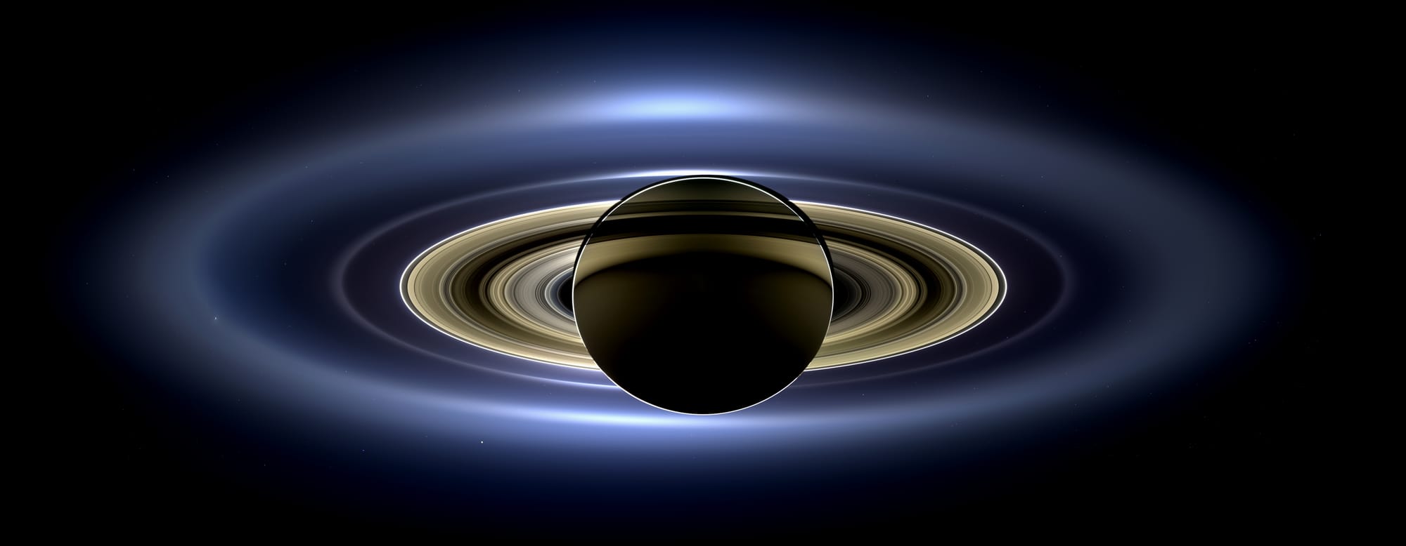 On July 19, 2013, in an event celebrated the world over, NASA's Cassini spacecraft slipped into Saturn's shadow and turned to image the planet, seven of its moons, its inner rings -- and, in the background, our home planet, Earth. 
With the sun's powerful and potentially damaging rays eclipsed by Saturn itself, Cassini's onboard cameras were able to take advantage of this unique viewing geometry. They acquired a panoramic mosaic of the Saturn system that allows scientists to see details in the rings and throughout the system as they are backlit by the sun. This mosaic is special as it marks the third time our home planet was imaged from the outer solar system; the second time it was imaged by Cassini from Saturn's orbit; and the first time ever that inhabitants of Earth were made aware in advance that their photo would be taken from such a great distance. 
With both Cassini's wide-angle and narrow-angle cameras aimed at Saturn, Cassini was able to capture 323 images in just over four hours. This final mosaic uses 141 of those wide-angle images. Images taken using the red, green and blue spectral filters of the wide-angle camera were combined and mosaicked together to create this natural-color view. A brightened version with contrast and color enhanced (Figure 1), a version with just the planets annotated (Figure 2), and an annotated version (Figure 3) are shown above. 
This image spans about 404,880 miles (651,591 kilometers) across.
The outermost ring shown here is Saturn's E ring, the core of which is situated about 149,000 miles (240,000 kilometers) from Saturn. The geysers erupting from the south polar terrain of the moon Enceladus supply the fine icy particles that comprise the E ring; diffraction by sunlight gives the ring its blue color. Enceladus (313 miles, or 504 kilometers, across) and the extended plume formed by its jets are visible, embedded in the E ring on the left side of the mosaic. 
At the 12 o'clock position and a bit inward from the E ring lies the barely discernible ring created by the tiny, Cassini-discovered moon, Pallene (3 miles, or 4 kilometers, across). (For more on structures like Pallene's ring, see PIA08328). The next narrow and easily seen ring inward is the G ring. Interior to the G ring, near the 11 o'clock position, one can barely see the more diffuse ring created by the co-orbital moons, Janus (111 miles, or 179 kilometers, across) and Epimetheus (70 miles, or 113 kilometers, across). Farther inward, we see the very bright F ring closely encircling the main rings of Saturn.
Following the outermost E ring counter-clockwise from Enceladus, the moon Tethys (662 miles, or 1,066 kilometers, across) appears as a large yellow orb just outside of the E ring. Tethys is positioned on the illuminated side of Saturn; its icy surface is shining brightly from yellow sunlight reflected by Saturn. Continuing to about the 2 o'clock position is a dark pixel just outside of the G ring; this dark pixel is Saturn's Death Star moon, Mimas (246 miles, or 396 kilometers, across). Mimas appears, upon close inspection, as a very thin crescent because Cassini is looking mostly at its non-illuminated face. 
The moons Prometheus, Pandora, Janus and Epimetheus are also visible in the mosaic near Saturn's bright narrow F ring. Prometheus (53 miles, or 86 kilometers, across) is visible as a faint black dot just inside the F ring and at the 9 o'clock position. On the opposite side of the rings, just outside the F ring, Pandora (50 miles, or 81 kilometers, across) can be seen as a bright white dot. Pandora and Prometheus are shepherd moons and gravitational interactions between the ring and the moons keep the F ring narrowly confined. At the 11 o'clock position in between the F ring and the G ring, Janus (111 miles, or 179 kilometers, across) appears as a faint black dot. Janus and Prometheus are dark for the same reason Mimas is mostly dark: we are looking at their non-illuminated sides in this mosaic. Midway between the F ring and the G ring, at about the 8 o'clock position, is a single bright pixel, Epimetheus. Looking more closely at Enceladus, Mimas and Tethys, especially in the brightened version of the mosaic, one can see these moons casting shadows through the E ring like a telephone pole might cast a shadow through a fog.
In the non-brightened version of the mosaic, one can see bright clumps of ring material orbiting within the Encke gap near the outer edge of the main rings and immediately to the lower left of the globe of Saturn. Also, in the dark B ring within the main rings, at the 9 o'clock position, one can see the faint outlines of two spoke features, first sighted by NASA's Voyager spacecraft in the early 1980s and extensively studied by Cassini.
Finally, in the lower right of the mosaic, in between the bright blue E ring and the faint but defined G ring, is the pale blue dot of our planet, Earth. Look closely and you can see the moon protruding from the Earth's lower right. (For a higher resolution view of the Earth and moon taken during this campaign, see PIA14949.) Earth's twin, Venus, appears as a bright white dot in the upper left quadrant of the mosaic, also between the G and E rings. Mars also appears as a faint red dot embedded in the outer edge of the E ring, above and to the left of Venus. 
For ease of visibility, Earth, Venus, Mars, Enceladus, Epimetheus and Pandora were all brightened by a factor of eight and a half relative to Saturn. Tethys was brightened by a factor of four. In total, 809 background stars are visible and were brightened by a factor ranging from six, for the brightest stars, to 16, for the faintest. The faint outer rings (from the G ring to the E ring) were also brightened relative to the already bright main rings by factors ranging from two to eight, with the lower-phase-angle (and therefore fainter) regions of these rings brightened the most. The brightened version of the mosaic was further brightened and contrast-enhanced all over to accommodate print applications and a wide range of computer-screen viewing conditions. 
Some ring features -- such as full rings traced out by tiny moons -- do not appear in this version of the mosaic because they require extreme computer enhancement, which would adversely affect the rest of the mosaic. This version was processed for balance and beauty.
This view looks toward the unlit side of the rings from about 17 degrees below the ring plane. Cassini was approximately 746,000 miles (1.2 million kilometers) from Saturn when the images in this mosaic were taken. Image scale on Saturn is about 45 miles (72 kilometers) per pixel.
This mosaic was made from pictures taken over a span of more than four hours while the planets, moons and stars were all moving relative to Cassini. Thus, due to spacecraft motion, these objects in the locations shown here were not in these specific places over the entire duration of the imaging campaign. Note also that Venus appears far from Earth, as does Mars, because they were on the opposite side of the sun from Earth.

The Cassini-Huygens mission is a cooperative project of NASA, the European Space Agency and the Italian Space Agency. NASA's Jet Propulsion Laboratory, a division of the California Institute of Technology in Pasadena, manages the mission for NASA's Science Mission Directorate, Washington, D.C. The Cassini orbiter and its two onboard cameras were designed, developed and assembled at JPL. The imaging operations center is based at the Space Science Institute in Boulder, Colo.