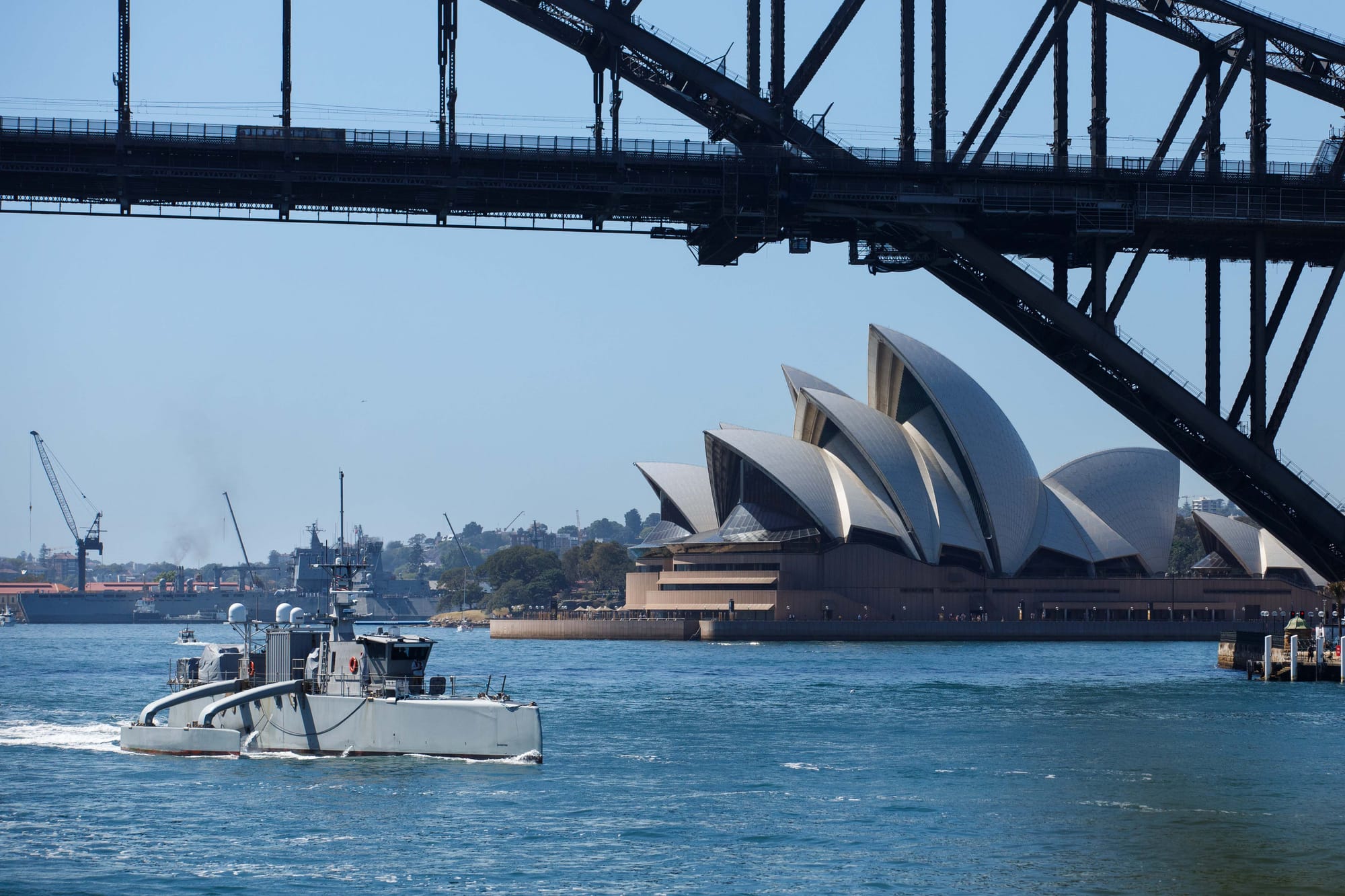 The unmanned surface vessel Sea Hunter transits underneath the Sydney Harbor bridge as part of a scheduled port visit during Integrated Battle Problem (IBP) 23.2, Oct 24, 2023. IBP 23.2 is a Pacific Fleet exercise to test, develop and evaluate the integration of unmanned platforms into fleet operations to create warfighting advantages. (U.S. Navy photo by Ensign Pierson Hawkins)
