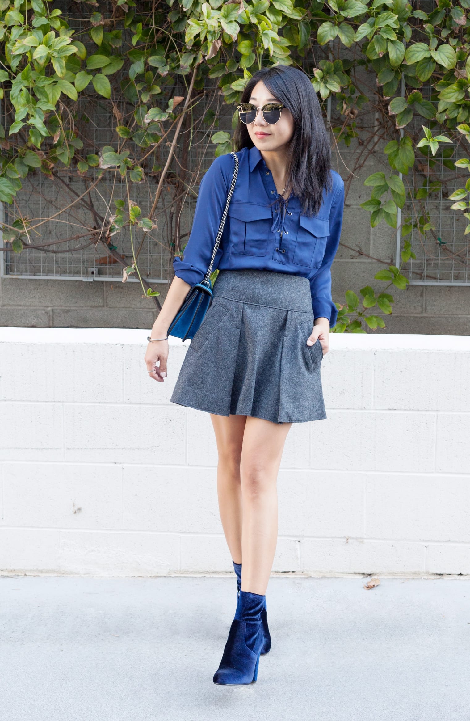 Woman standing outdoors wearing sunglasses, a blue blouse, a wool mini skirt, and ankle boots.