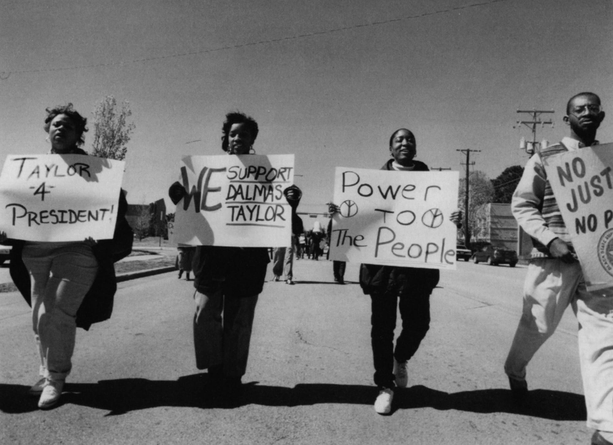 African-American students holding signs and marching to support Provost Taylor to be appointed University of Texas at Arlington interim president when President Amacher resigned.