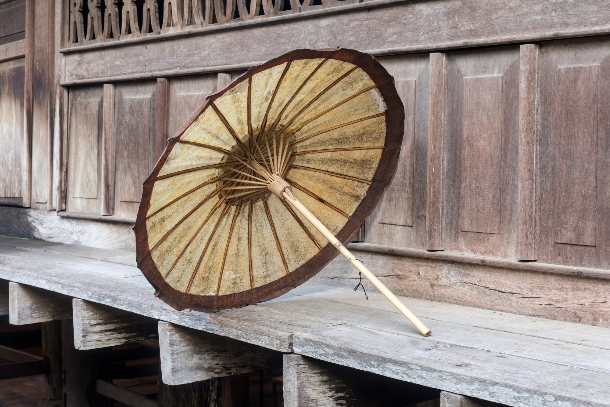 Beige and brown Lao oil-paper umbrella placed on the edge of a wooden house, at Heuan Chan heritage house, Luang Prabang, Laos.