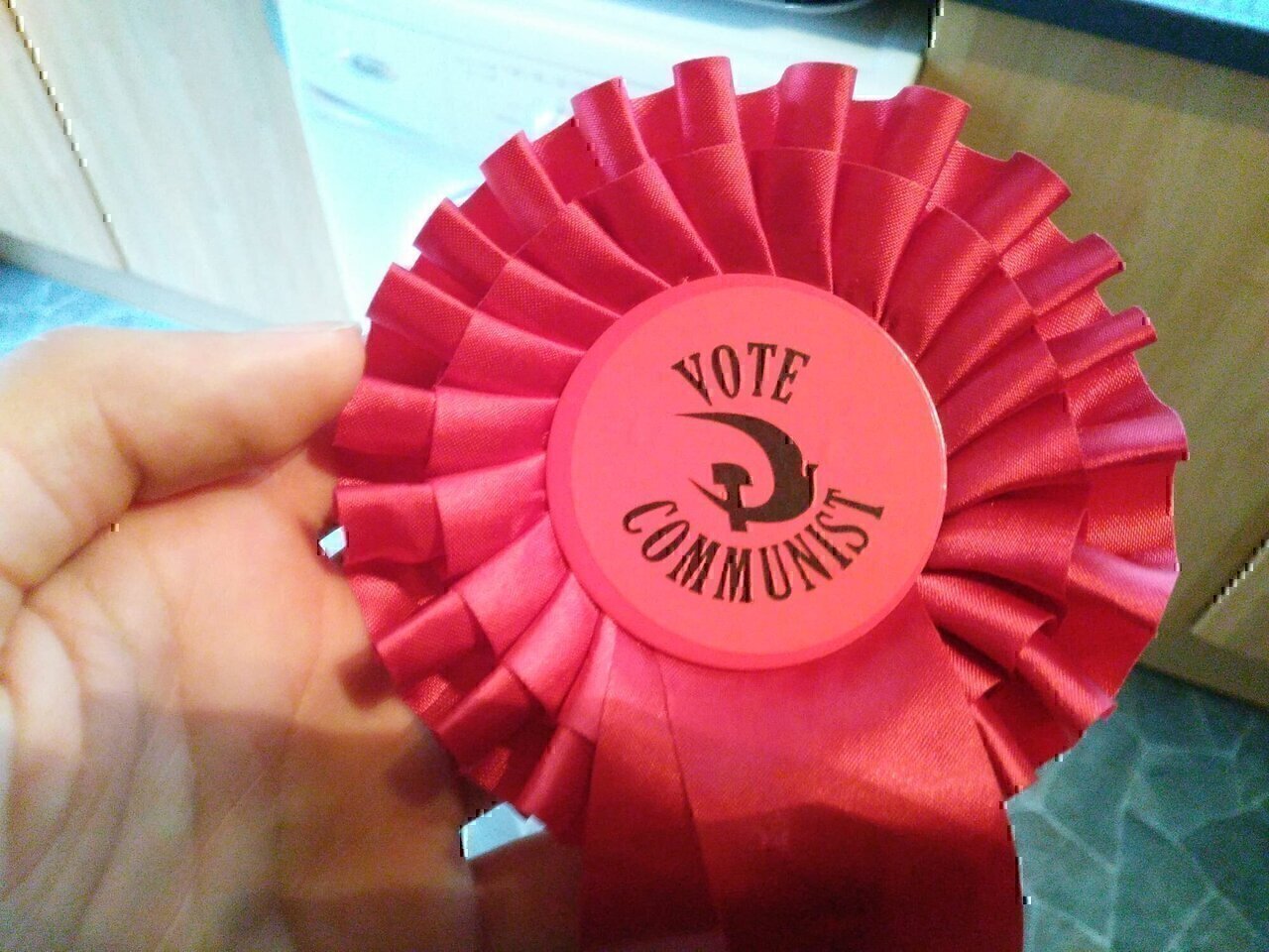 Red rosette with a hammer and dove and the words 'Vote Communist'