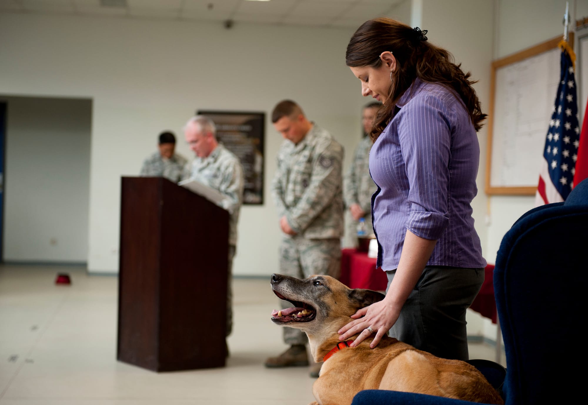 Stacey Ball, owner of former military working dog, Max, pets the dog to keep him calm during the invocation at his retirement ceremony March 23, 2012 in the 39th SFS guardmount room. Max now lives with Mrs. Ball and her husband, Staff Sgt. Joshua Ball, 39th Maintenance Squadron.