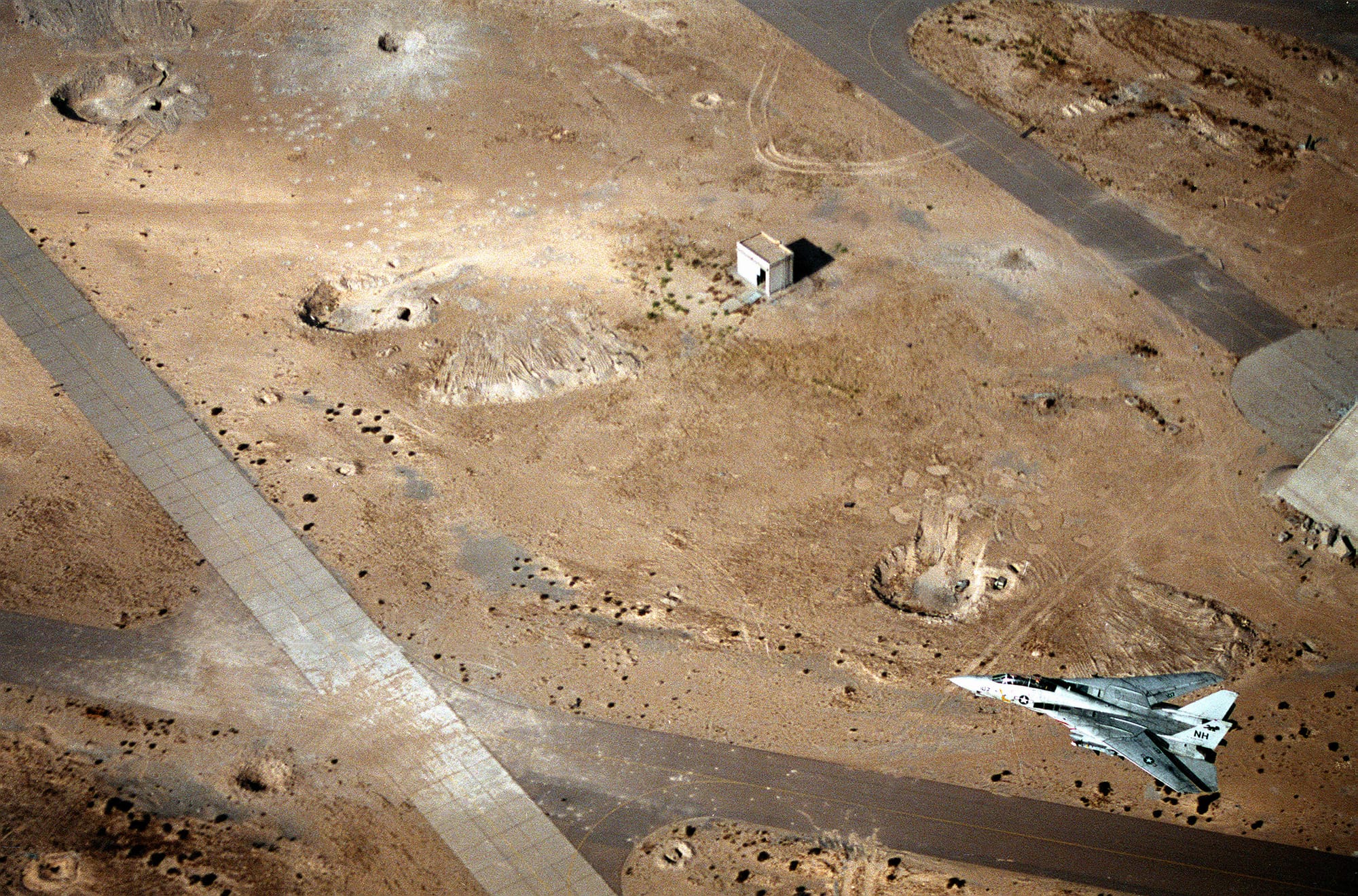 A U.S. Navy Grumman F-14A Tomcat from Fighter Squadron 114 (VF-114) "Aardvarks" flies over Achmed Al Jaber air base, Kuwait. The airfield was heavily damaged during the 1991 Gulf War. VF-114 was assigned to Carrier Air Wing 11 (CVW-11) aboard the aircraft carrier USS Abraham Lincoln (CVN-72) for a deployment to the Western Pacific and the Indian Ocean from 28 May to 25 November 1991. This was VF-114's last deployment before being disestablished on 30 April 1993.