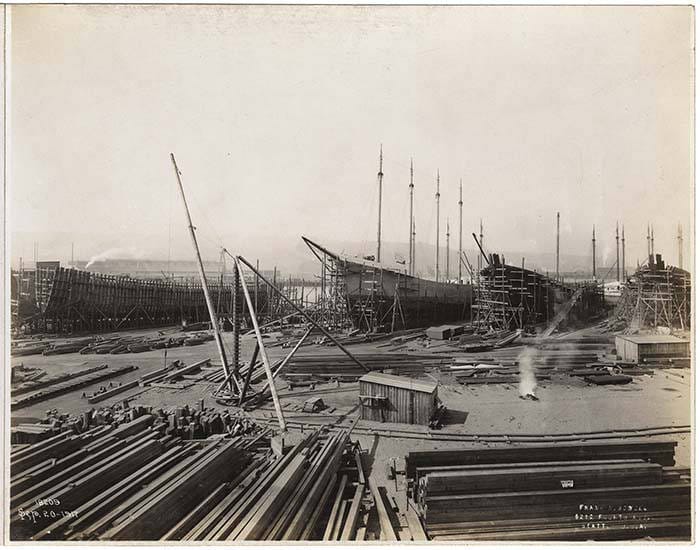 This view of the Puget Sound Bridge & Dredging Company shipyard, taken on September 20, 1917 shows a four-masted schooner and other vessels under construction. The yard is filled with stacks of heavy milled lumber from the Pacific Northwest's huge trees. Shipyard workers used the hoists (left center) to lift the lumber and move it from one place to another. 
This photograph is part of an album of Puget Sound Bridge & Dredging Co. projects; many of their projects were documented by noted Seattle photographer Frank H. Nowell. Puget Sound Bridge & Dredging Company (later Lockheed Shipbuilding and Construction Company) was established in Seattle in 1889 as a branch of the San Francisco Bridge Company. In its earlier days, the firm built many wooden ships, including sternwheeled steamboats for the Yukon gold rush and multi-masted freighters. 
Inscribed on negative: SEP.20-1917
Embossed on recto: Frank H. Nowell, 1212 Fourth Ave., Seattle, U. S. A.
Subjects (LCTGM): Boat & ship industry--Washington (State)--Seattle; Puget Sound Bridge & Dredging Company