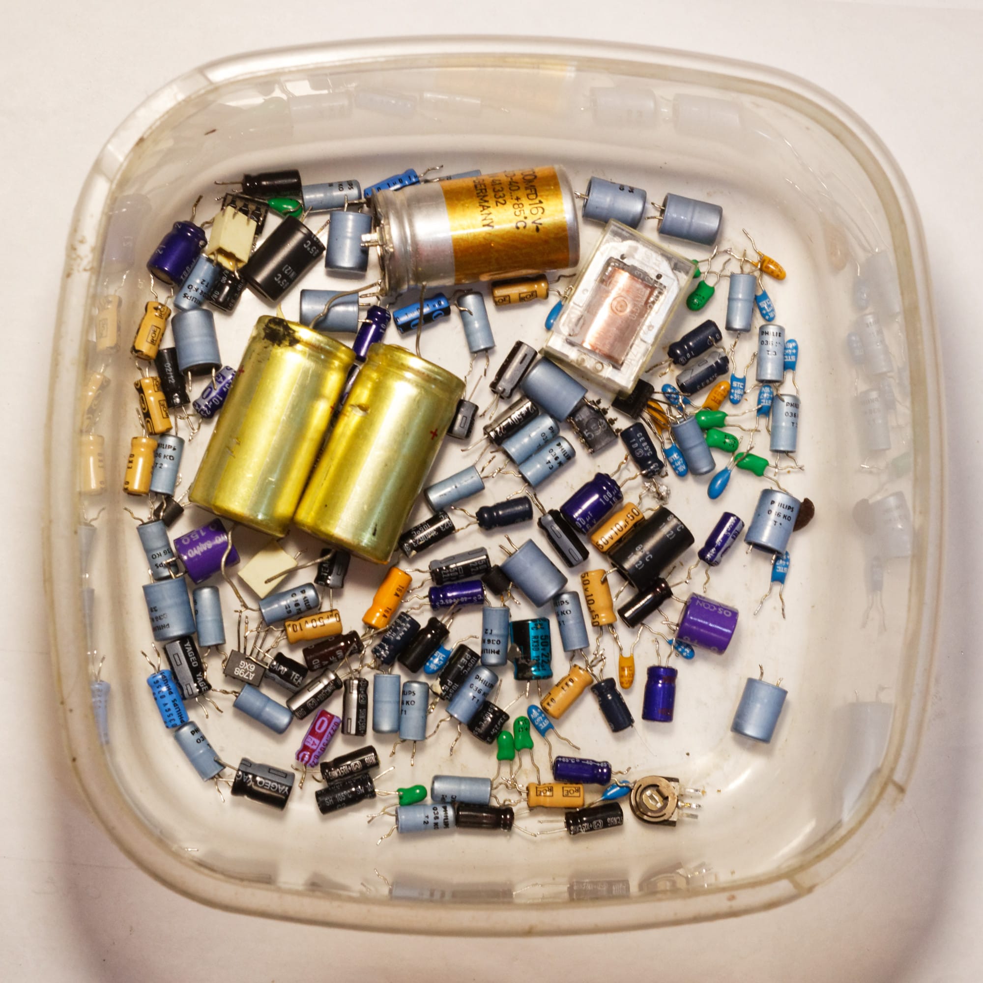 Capacitors and some other parts removed from the Revox B215 cassette deck. The pale blue and orange small electrolytics are factory original; deep blue and blacks were later replacements. The smallest green, yellow and blue blobs are factory original tantalums. Now, it's all e-waste.