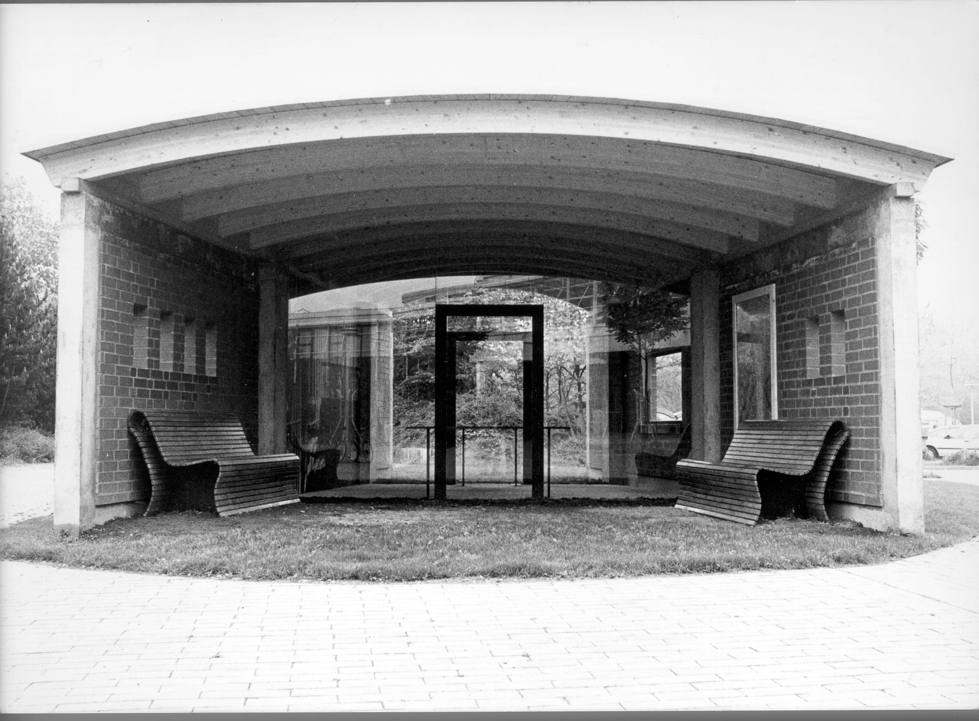 masonry, glass, benches, steel, map, photo
Getrud Luckner Trade School Freiburg, 1995
The artwork on the schoolyard grounds is not an actual bus stop. But at first glance it looks like one. It does not immediately reveal itself as a work of art. The masonry corresponds to that of the school buildings. Moreover, the work of art can be used (benches). Only the interior, with a steel table and a wall-filling large photo, can only be viewed but not entered. The benches are reflected inward through the glass walls that separate them from the interior. The building reconstructs, with reference to Gertrud Luckner, namesake of the school and honorary citizen of the city of Freiburg, the formal language of railroad carriages and waiting halls and is dedicated to the memory of Mrs. Luckner. 
Always on the move for her fellow human beings, Gertrud Luckner herself was arrested one day by Nazis on a train and deported to a concentration camp. Her restless, ultimately rushed life for others found pictorial expression in the resting place of the 'Haltestelle'. A work that also gives pictorial form to the temporary stay of young people at the school: In a unique and special way it invites to use the space it offers in a communicative way and to animate it.

Translated with www.DeepL.com/Translator (free version)